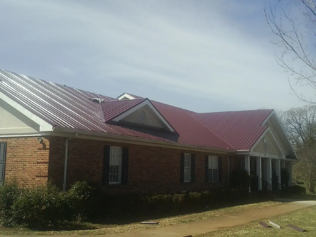 Red metal roof with gabled entries on a long brick building, from a Hail Damage Roof Repair job in West Warwick