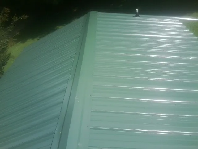 New green metal panels meeting at the ridge of a roof — Flat Roof Repair work by our crew in West Warwick