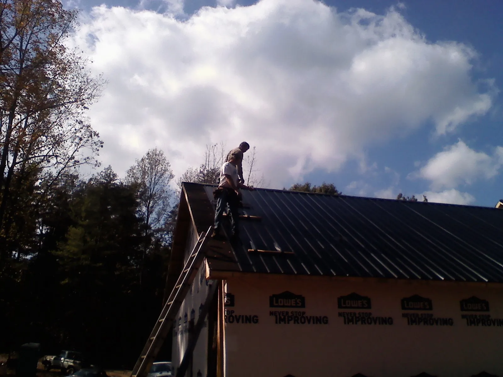 Roofer fastening dark metal panels high against a cloudy sky, from a Roof Inspection job in West Warwick