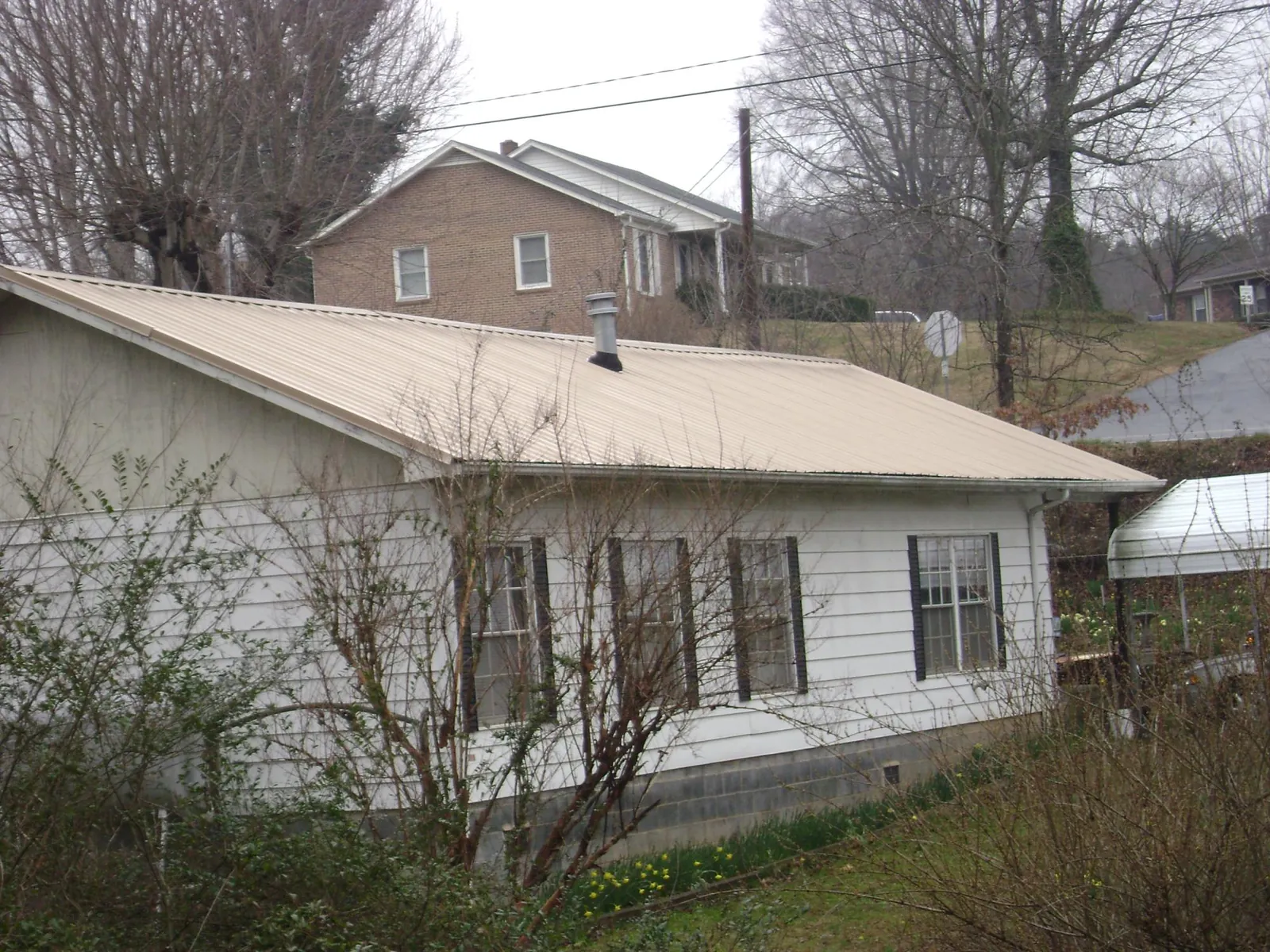 Tan metal roof on a white sided house set into a hillside — Commercial Roofing by Roofing Brothers in West Warwick
